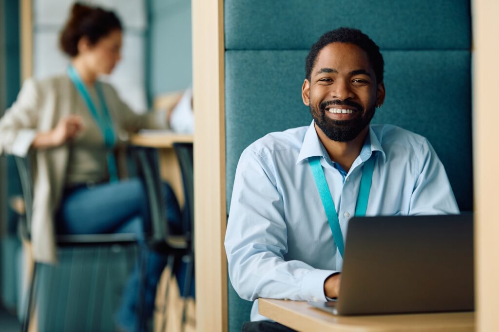 Happy black manager working on laptop in the office and looking at camera.